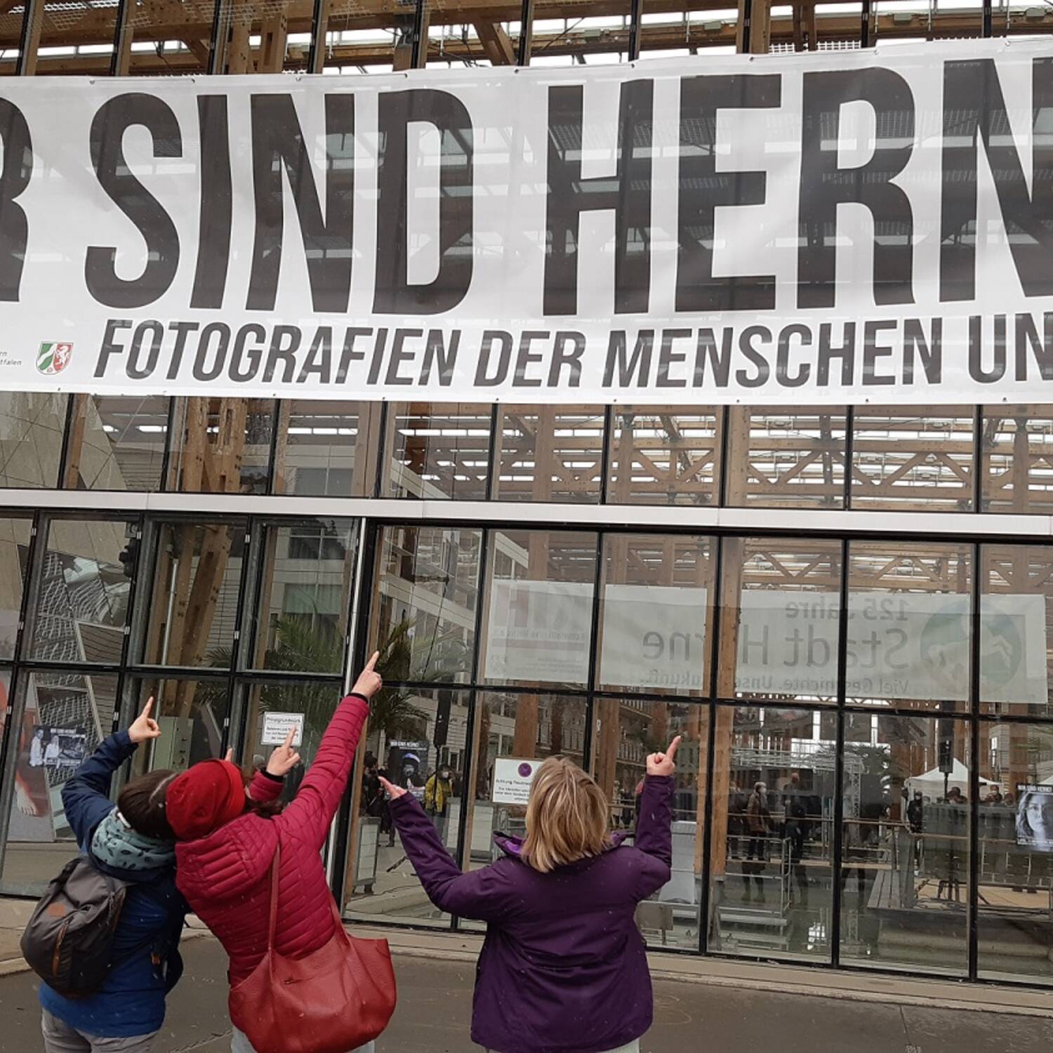 Drei Personen zeigen auf einen großen Banner WIR SIND HERNE
