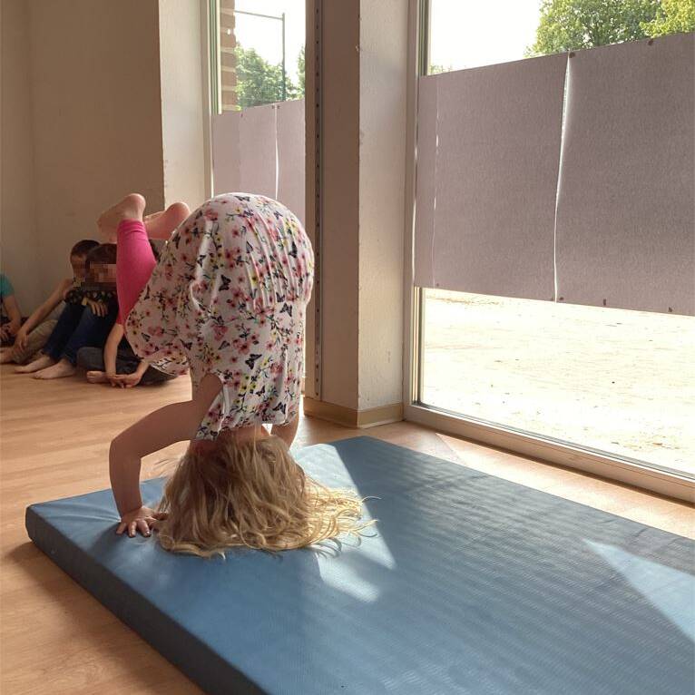 Ein Mädchen im Kleid macht einen Purzelbaum auf einer blauen Matte.