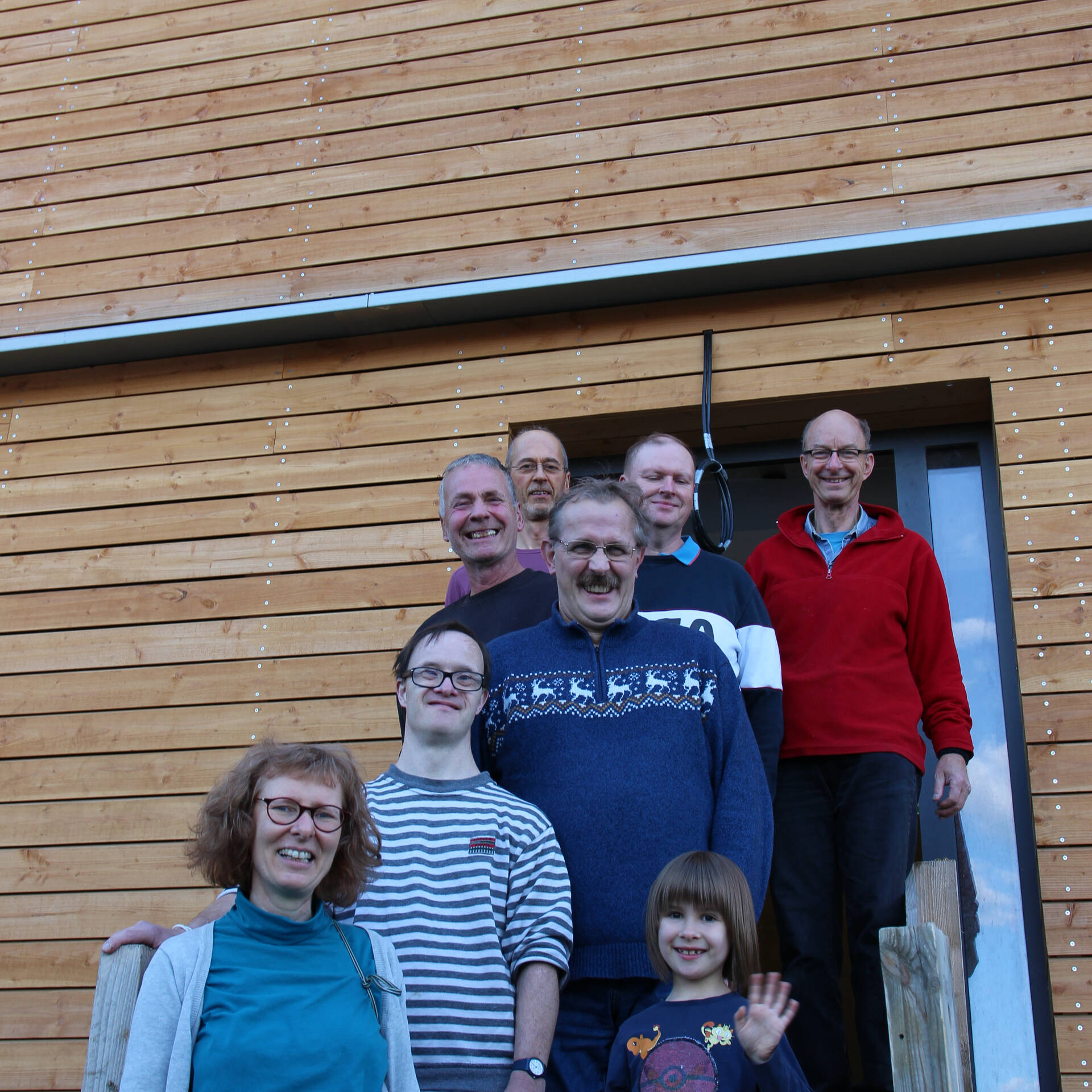 Mehrere Personen stehen auf einer Treppe und ein Kind winkt.