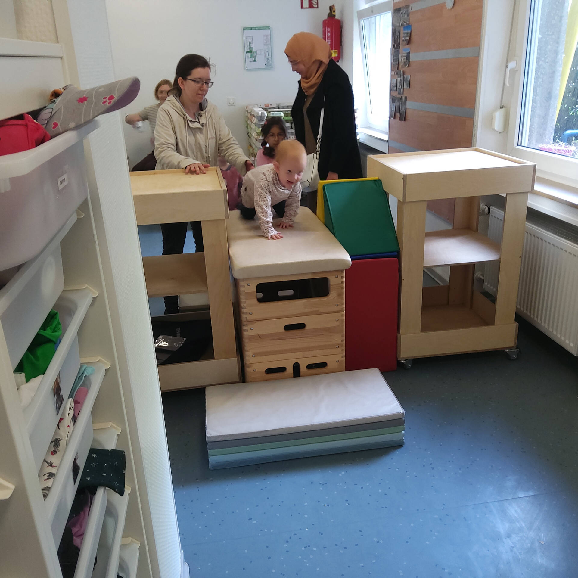 Ein Kind krabbelt über einen Bock und zwei Frauen stehen daneben.