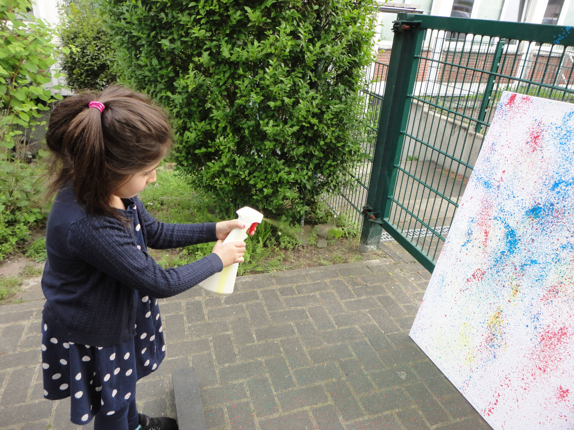 Ein Mädchen spritzt mit Frabe auf eine weiße Fläche