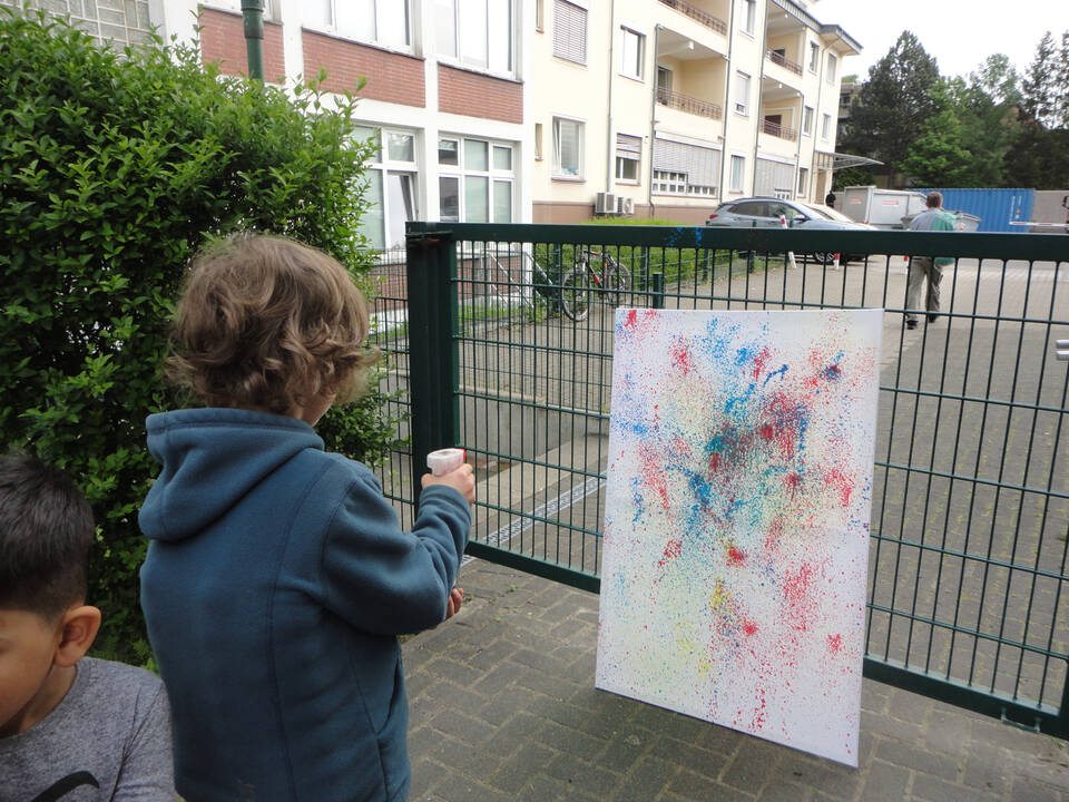 Ein Kind spritzt mit Frabe auf eine weiße Fläche