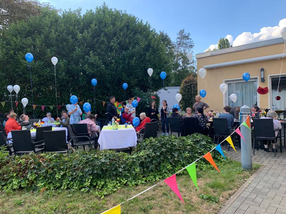Viele Personen draussen in einem Garten der geschmückt ist.
