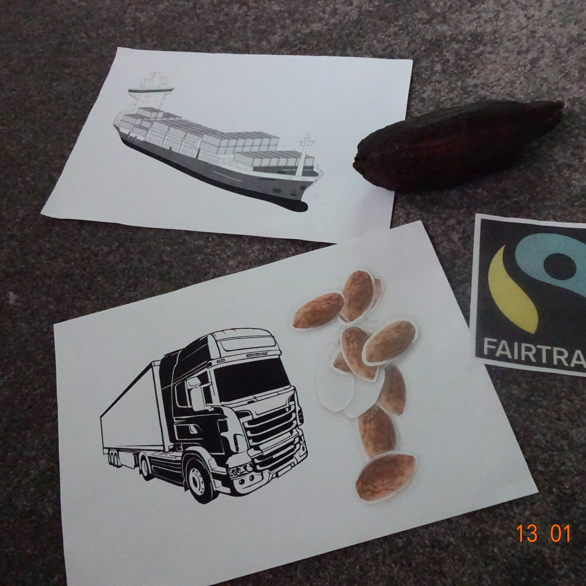 Ein Logo von Fair Trade und jeweils ein Bild mit einem Zug und einem LKW liegt auf dem Boden.