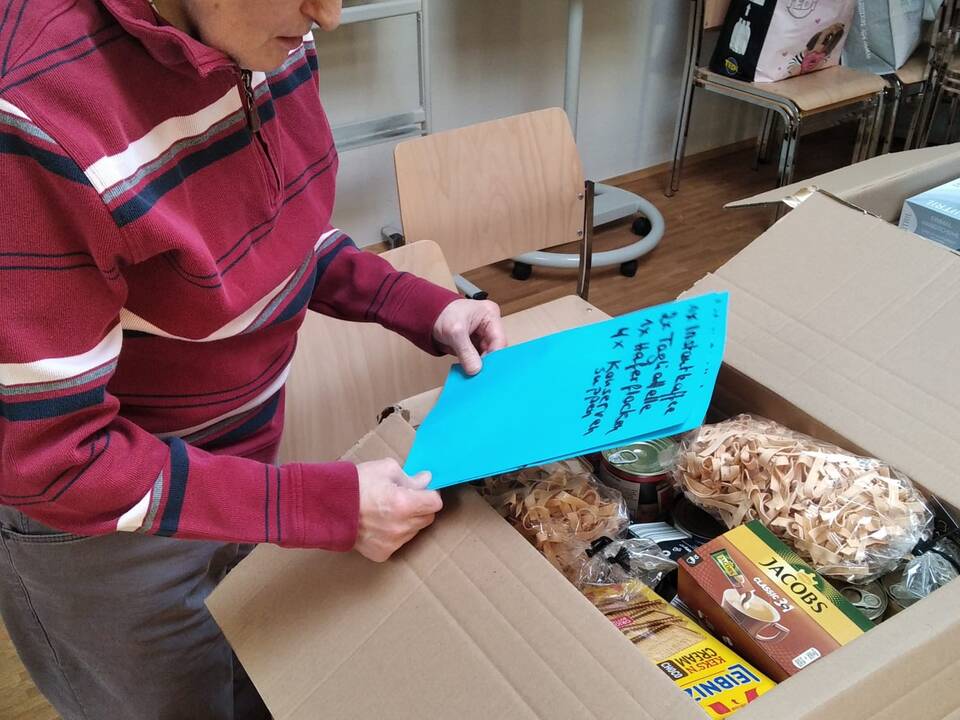 Ein Mann hält einen Zettel in der Hand, ein Paket steht vor ihm.