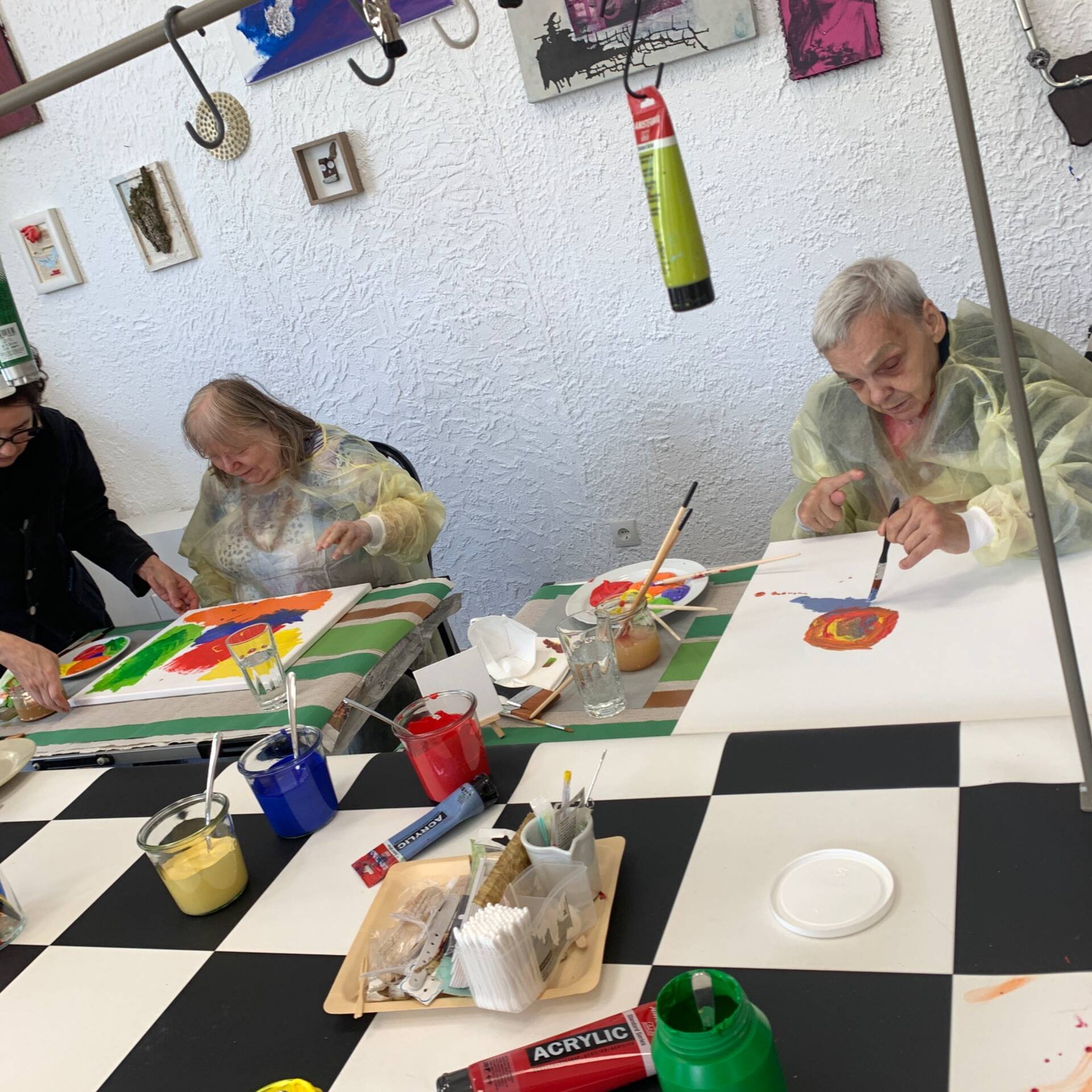 Zwei Personen malen Bilder, eine Frau hilft.