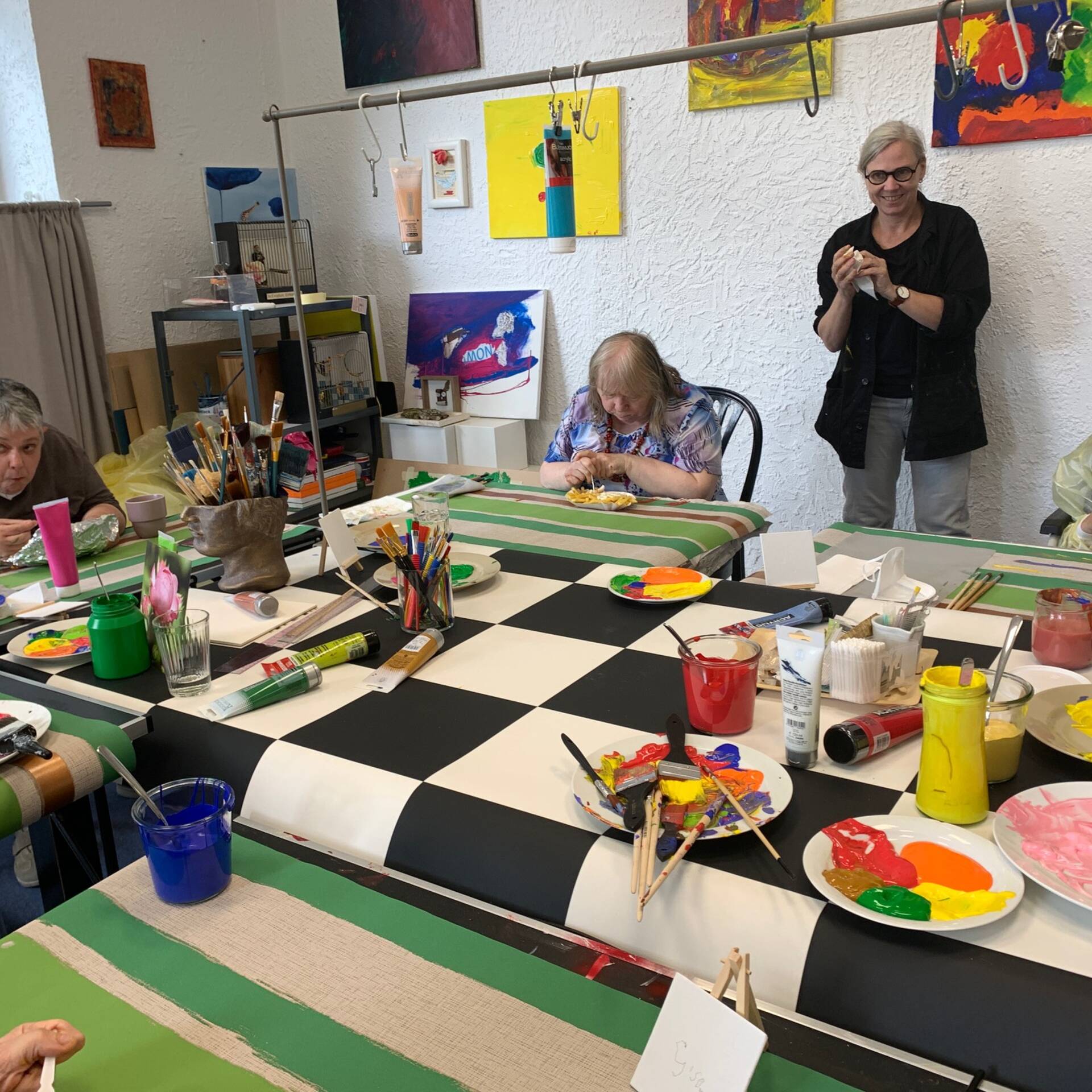 Mehrere Menschen malen an einem Tisch, eine Frau steht dahinter.