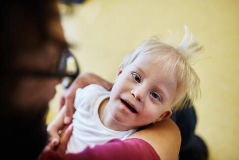 Ein Kind liegt in den Armen einer Person und lacht.