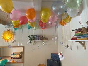 Ballons schweben unter der Decke, daran sind Zettel befestigt.
