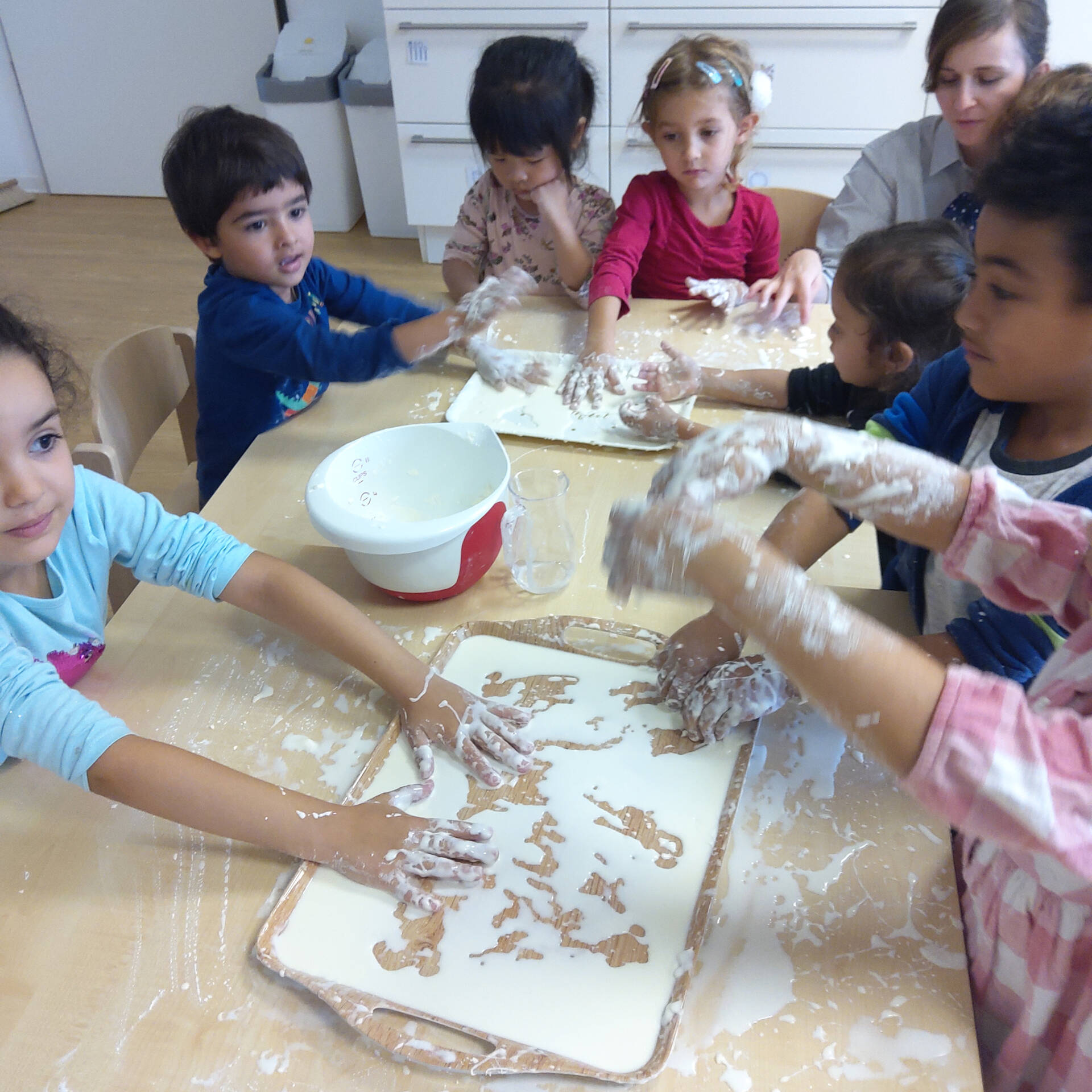 Mehrere Kinder sitzen am Tisch und Mischen Wasser und Speisestärke mit den Händen.