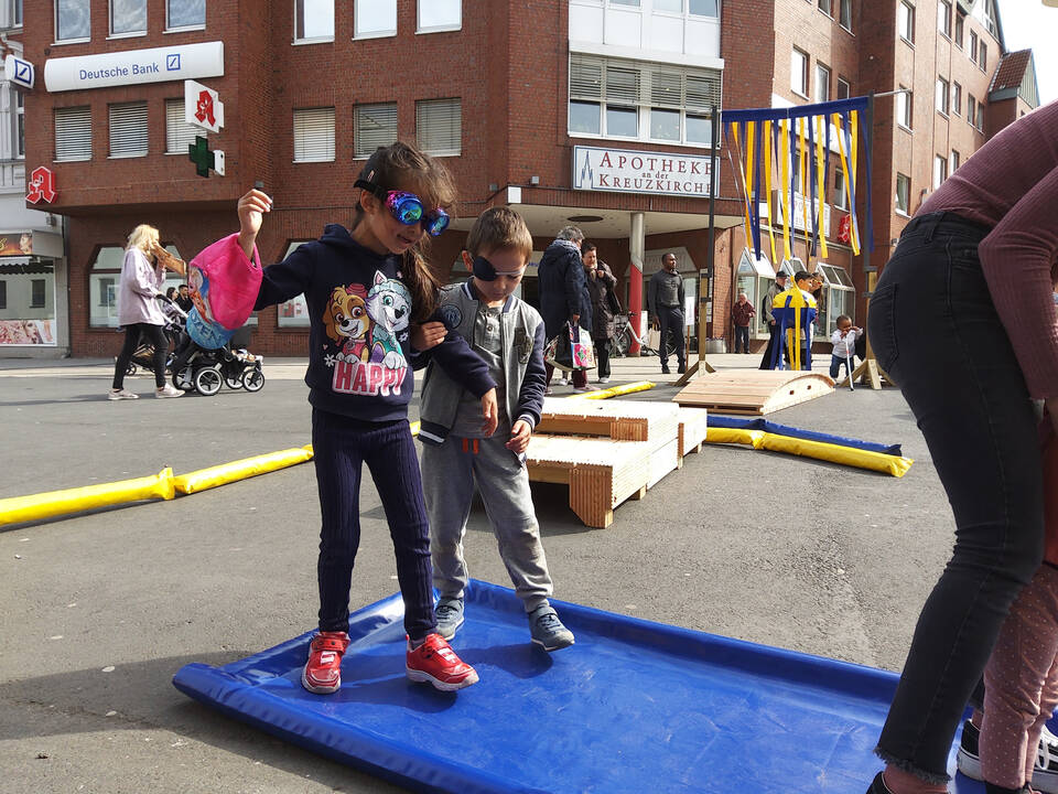 Ein Kind mit einer Augenklappe führt ein anderes Kind mit sichtschutz über ein Hinderniss.