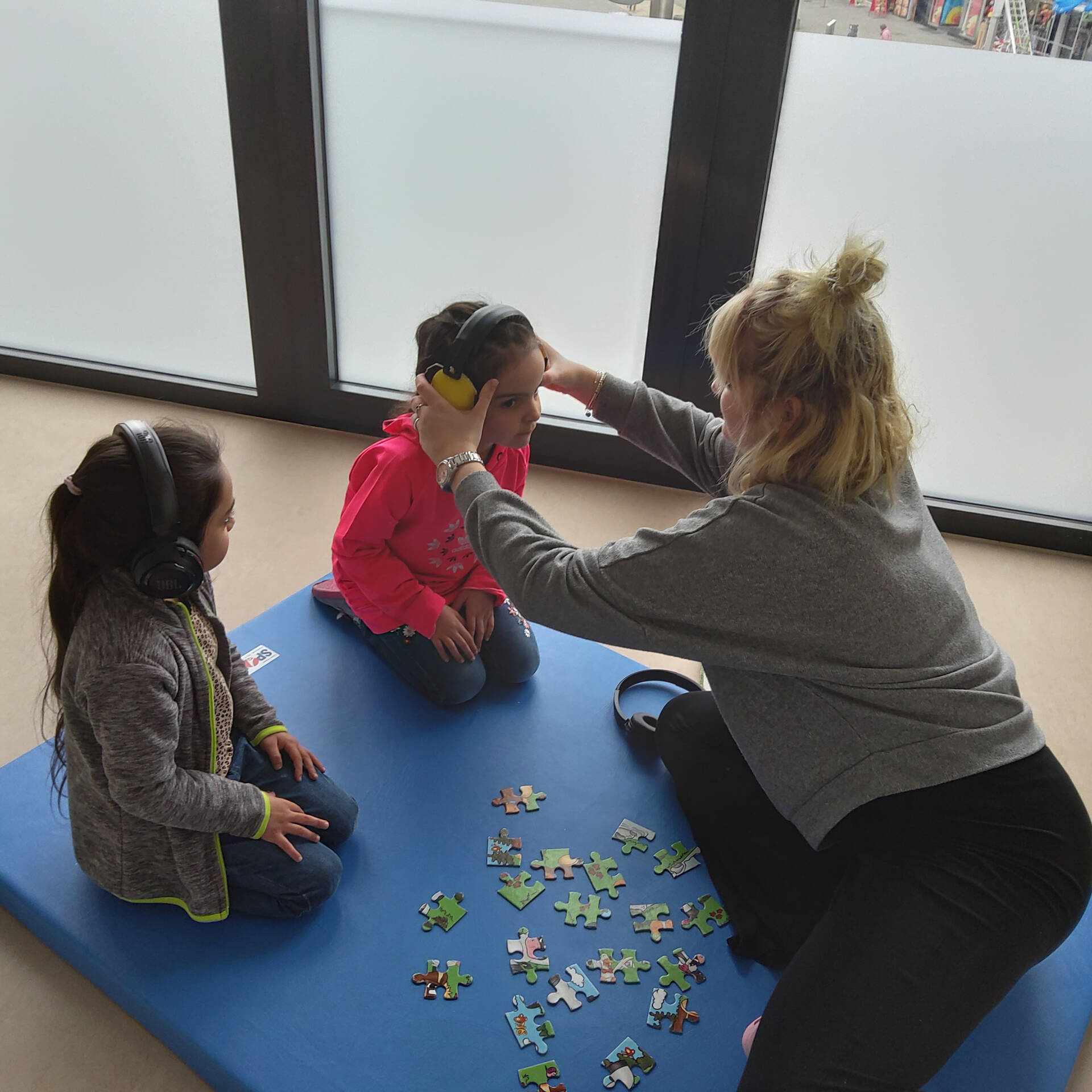 Zwei Kinder, eins hat Kopfhörer auf dem Kopf, das Andere bekommt gerade welche angezogen.