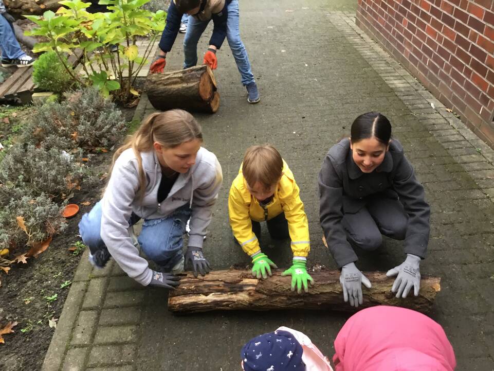 Kinder und Jugendliche rollen kleine Baumstämme