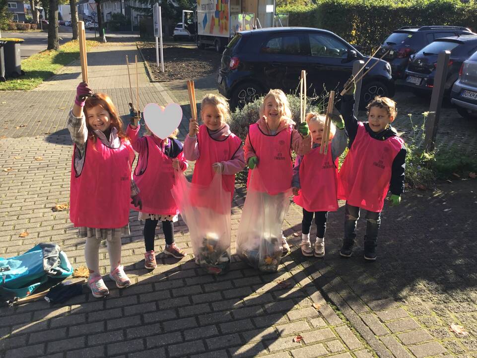 Kinder auf einem Bürgersteig mit Müllzangen in der Hand, die sie nach oben halten.