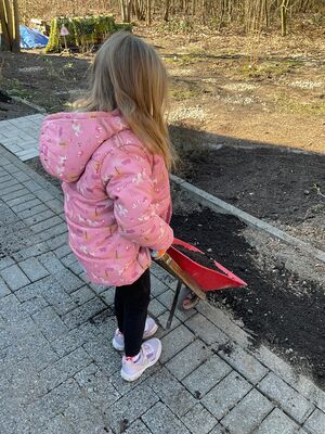 Ein Kind kippt Erde von einer Schubkarre in ein Beet.