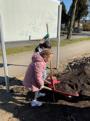 Zwei Kinder fahren mit einer Schubkarre voll Dreck umher.