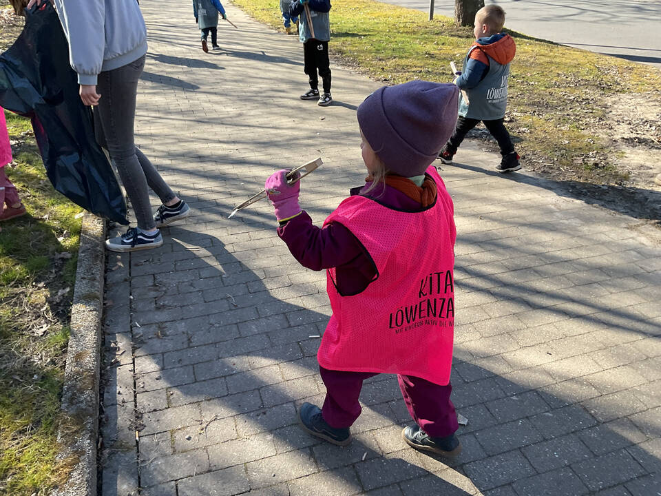 Ein Kind trägt Müll mit einer Zange zum Müllsack.