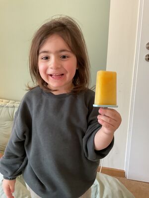 Ein Kind hält ein oranges Eis in der Hand. 