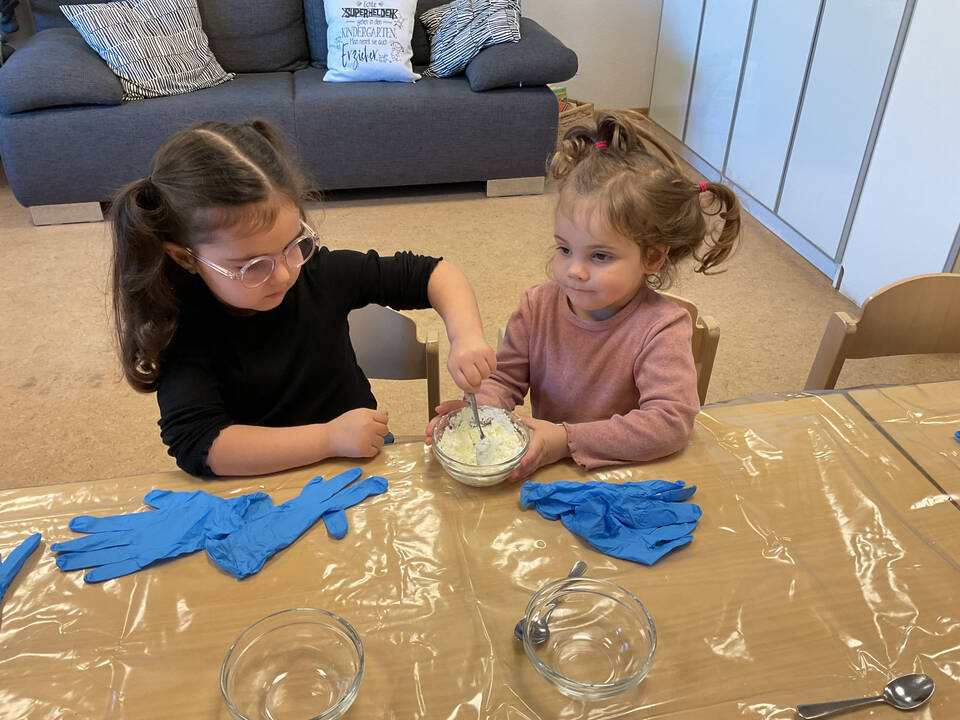 Zwei Kinder sitzen an einem Tisch und verrühren etwas.