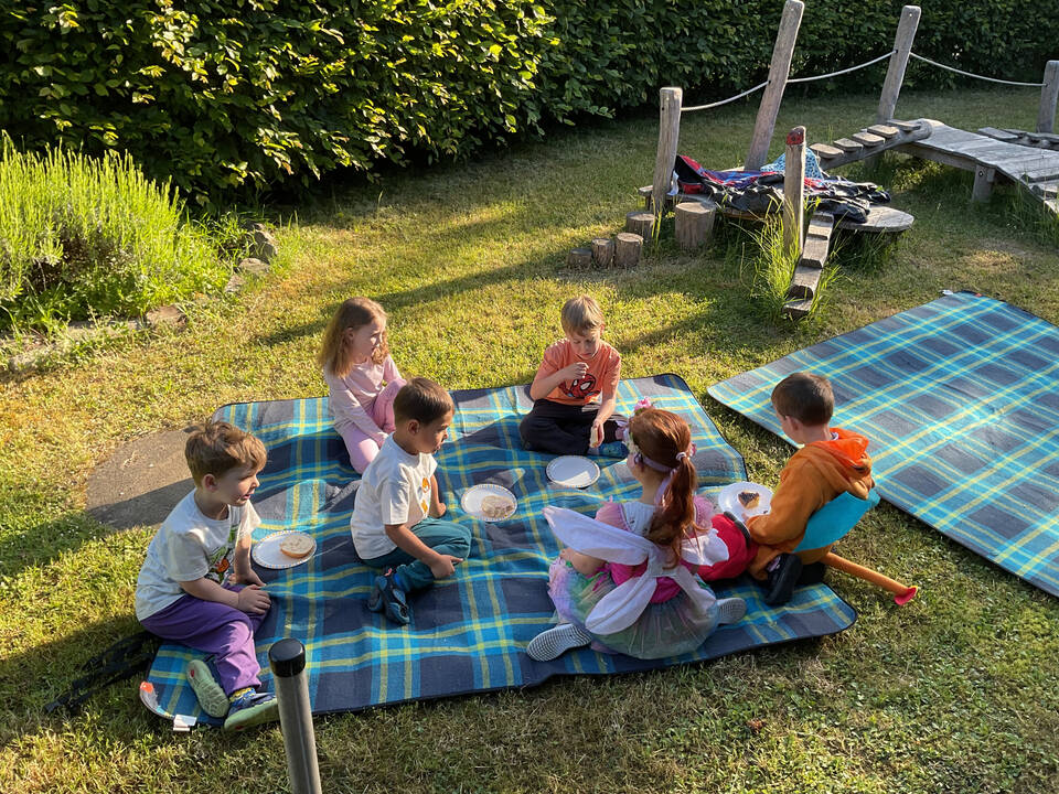 Kinder sitzen auf einer Picknikdecke und essen.
