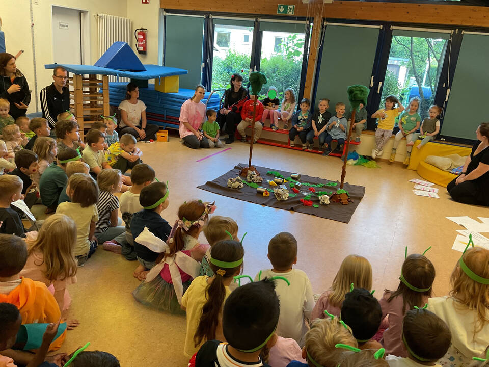 Viele Kinder sitzen im Kreiss in einem Raum, um ein Schaubild herum.