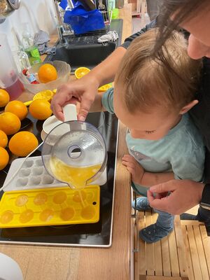 Ein Kind macht mit einer erwachsenen Person Eiswürfel aus Orangensaft.