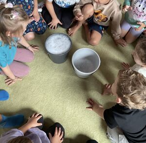 Kinder sitzen um 2 Eimer mit Seifenwasser herum.