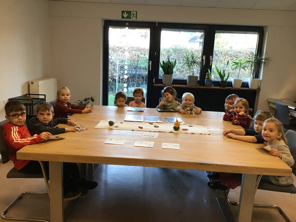 Elf Kinder sitzen zusammen an einem großen Tisch in einem Raum.