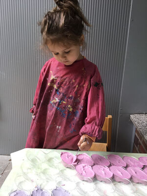 Ein Mädchen füllt die rosa Masse mit einem Löffel in eine Kunststoffform.