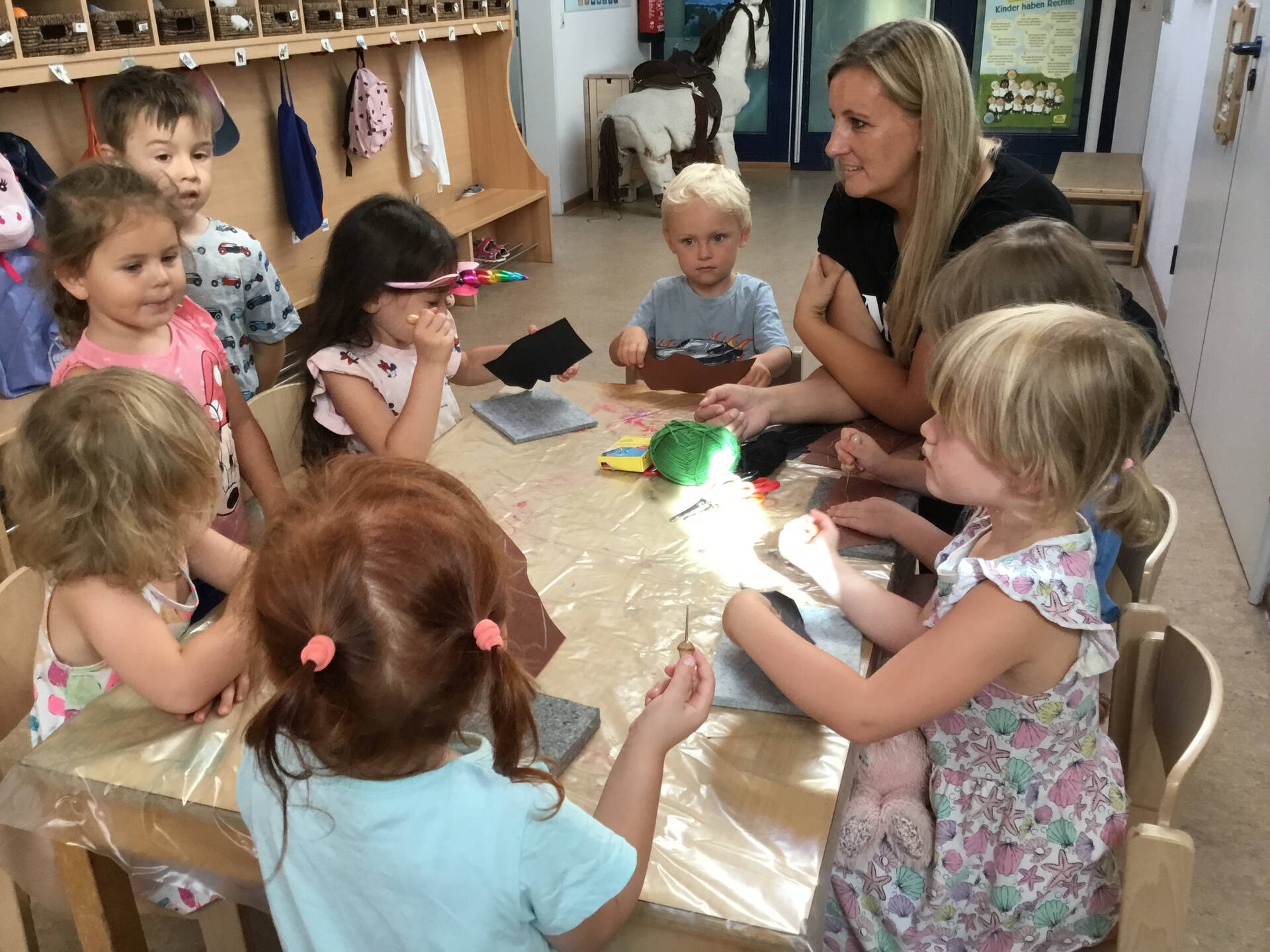 Kinder sitzen mit einer Erzieherin am Tisch.