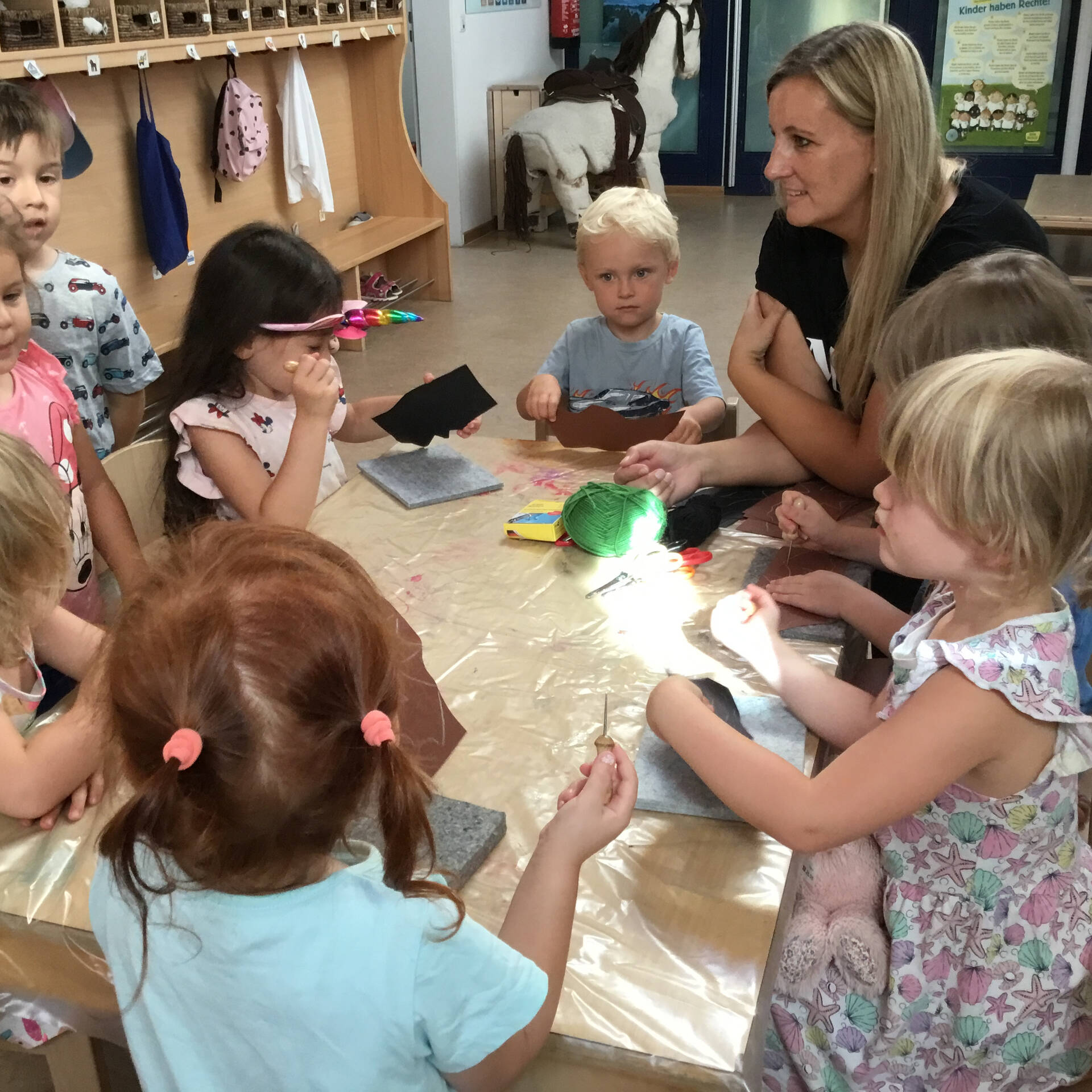 Kinder sitzen mit einer Erzieherin am Tisch.