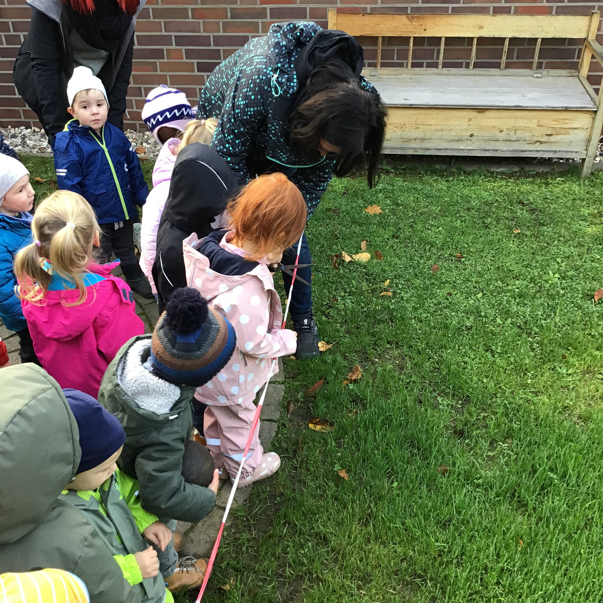Kinder stehen hinter einem Absperrband und eine Frau hilft es mit einer Schere durchzuschneiden.