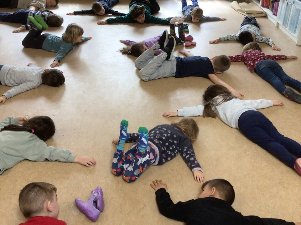 Mehrere Kinder liegen auf dem Bauch in einem Raum und strecken die Arme vom Körper weg.