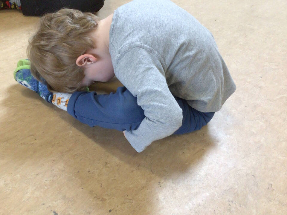 Ein Kind sitzt auf dem Boden und senkt seinen Oberkörper auf die Beine