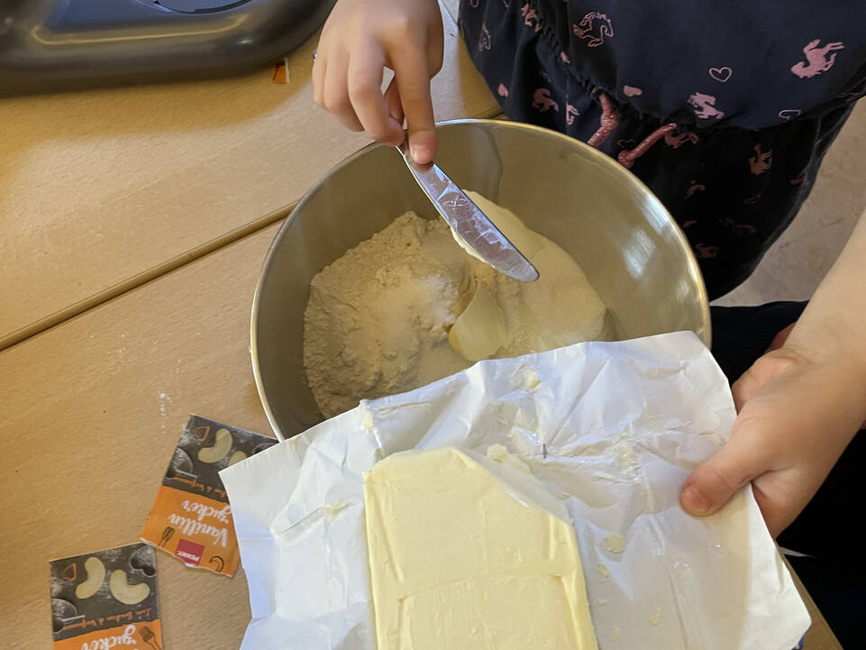 Kinderhände fügen Butter in eine Schüssel mit Zutaten.