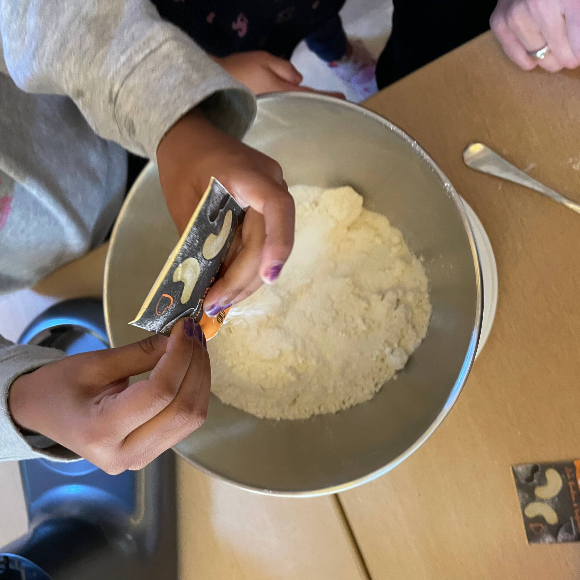 Kinderhände fügen weitere Zutaten in eine Schüssel mit Zutaten.