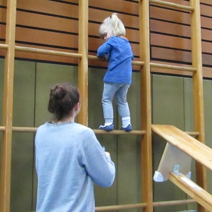 Ein Kind kletter die Sprossenwand hoch, eine Frau steht daneben.