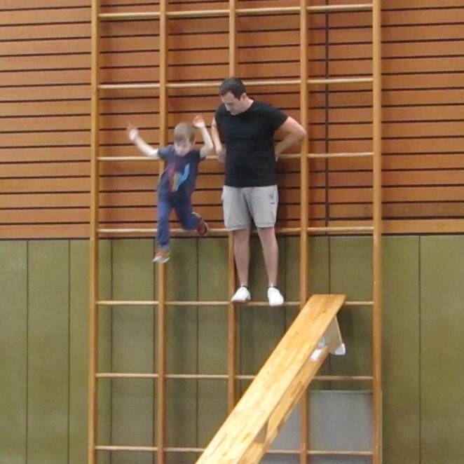Ein Kind und ein junger Mann stehen auf einer Sprossenwand.