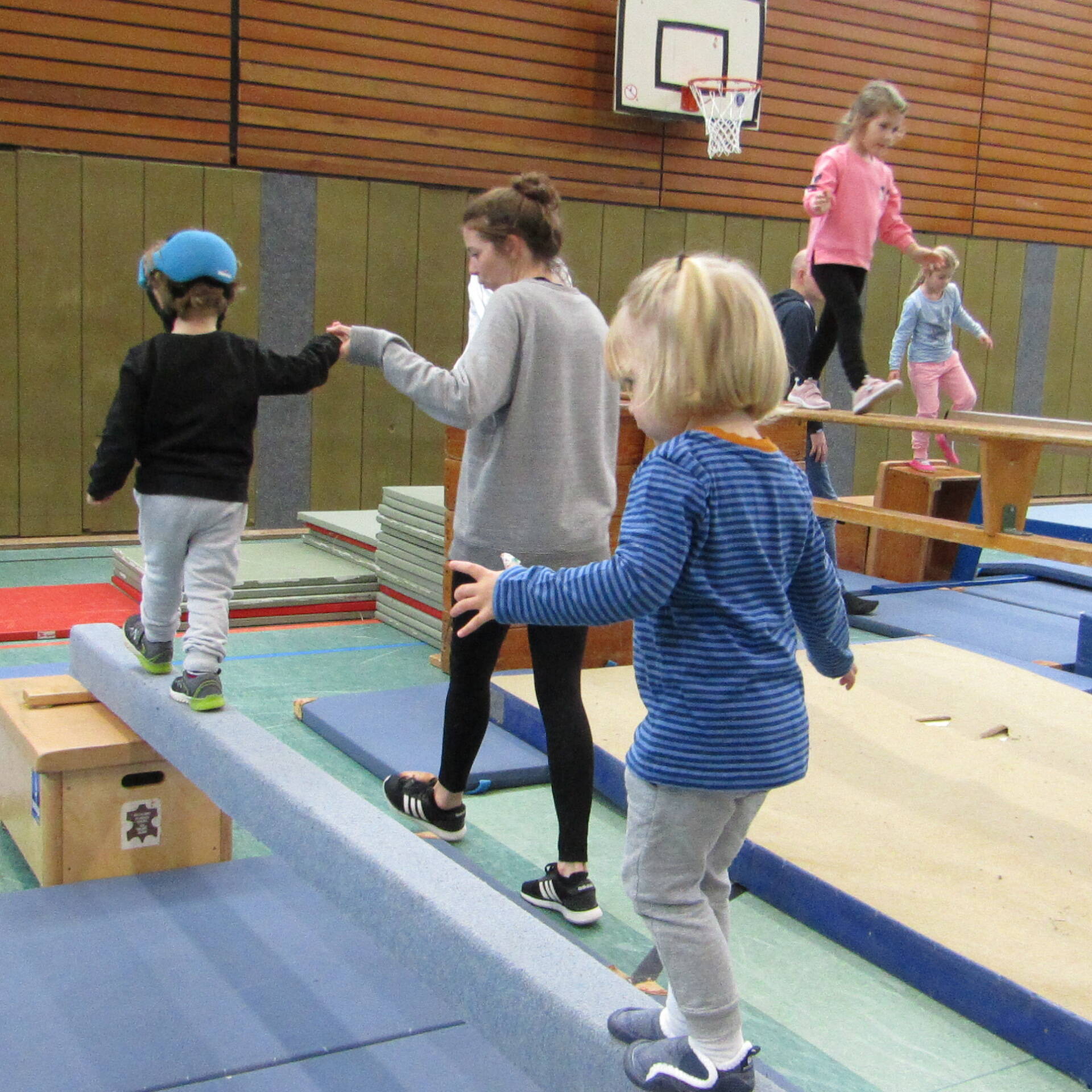 Zwei Kinder balancieren, ein Kind hält dabei die Hand einer jungen Frau.