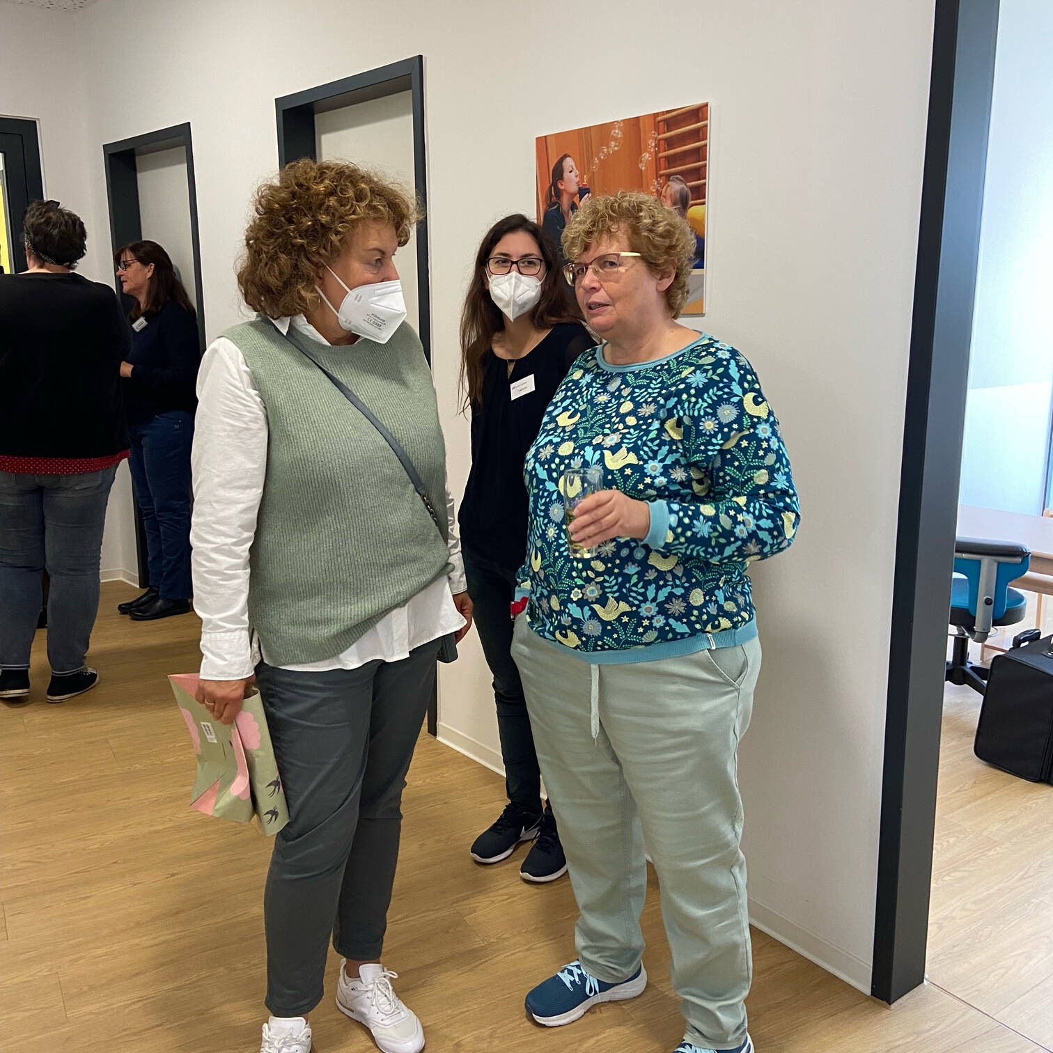 Drei Frauen stehen zusammen, zwei mit Maske.