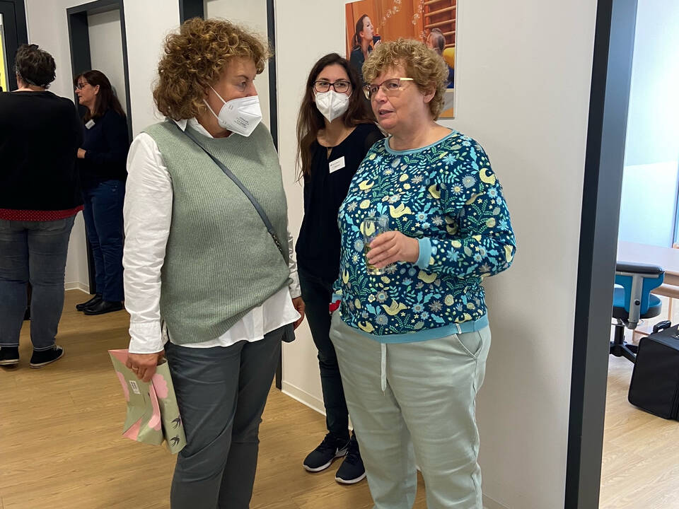 Drei Frauen stehen zusammen, zwei mit Maske.