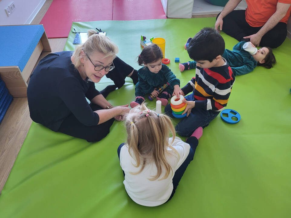 Kinder sitzen mit einer Frau auf einer Matte auf dem Boden.