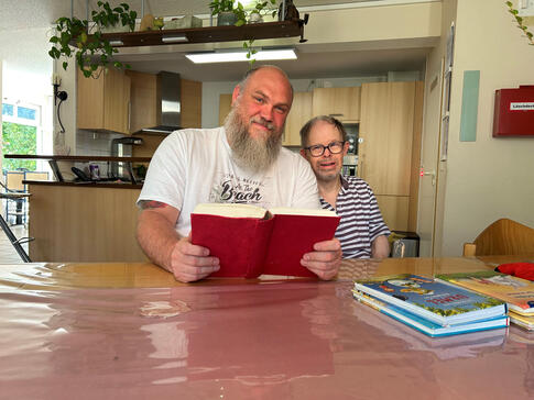 Sascha Seidel sitzt neben einem Mann und hält ein Buch in der Hand