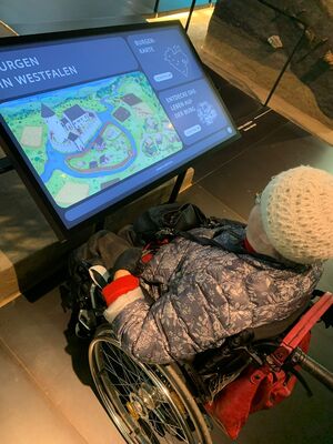 Eine Person im Rollstuhl schaut auf einen Monitor mit Informationen.