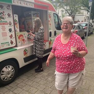 Eine Frau mit einem Eisbecher und dem Eiswagen im Hintergrund.