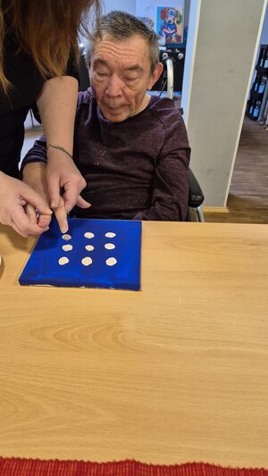 Ein Mann sitzt am Tisch und bekommt Hilfe bei der Gestaltung seines Bildes.