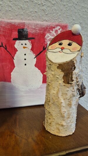 Ein Bild mit einem Schneemann und ein Birkenstamm bemalt mit einem Nikolausgesicht.