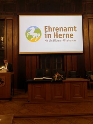 Ein Monitor in einem großen Raum mit einem Bild und den Worten Ehrenamt in Herne.