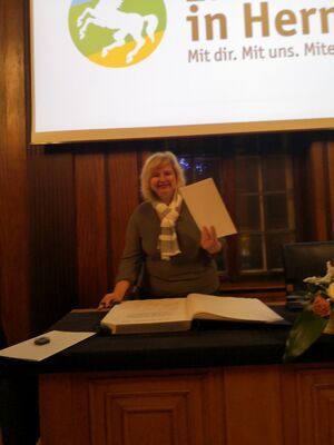 Eine Frau mit einem großen Blatt und vor einem großen Buch.