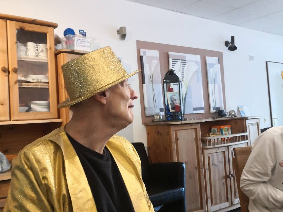 Ein Mann im goldenen Sakko und goldenem Hut an einem Tisch.